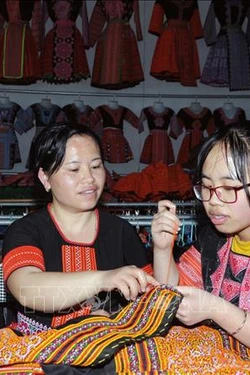 Chị Tráng Thị Dua (bên trái) truyền dạy nghề thêu, may truyền thống của đồng bào dân tộc Mông cho con gái. Ảnh: Quang Quyết-TTXVN
