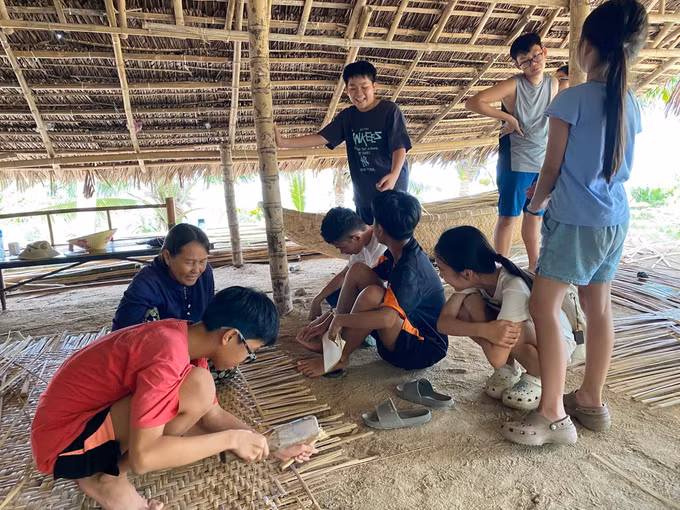 Các em nhỏ hào hứng trải nghiệm nghề đan lát truyền thống của người dân Gò Cỏ. Ảnh: TTXVN phát