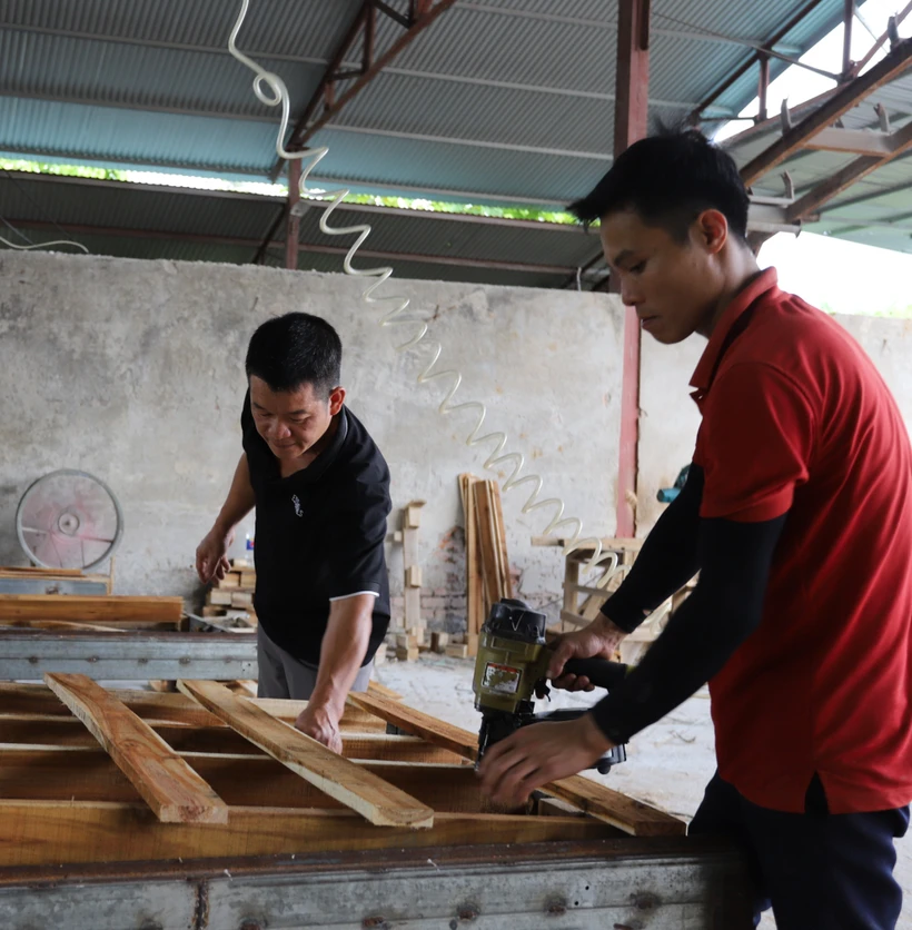 Anh Phùng Bình Minh (mặc áo đen) hướng dẫn công nhân kỹ thuật đóng tấm Pallet. Ảnh: Tiến Khánh - TTXVN