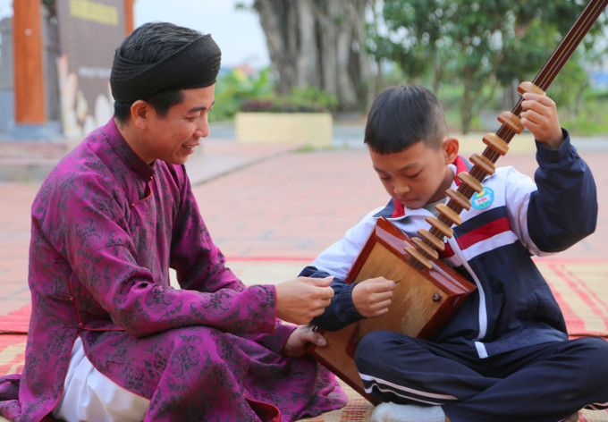 Nghệ nhân Ưu tú Tô Văn Tuyên, Chủ nhiệm Câu lạc bộ ca trù Đông Môn, hướng dẫn học sinh Trường Tiểu học Hòa Bình chơi đàn đáy.