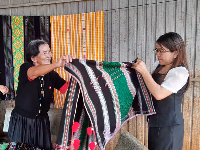 Bà Thị Y Rơ (76 tuổi, người dân tộc M’nông) giới thiệu tấm thổ cẩm đã hoàn chỉnh cho chuyên viên phòng văn hóa-xã hội xã Bù Gia Mập.