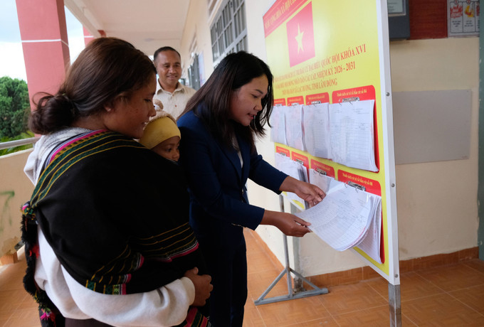 Chị Dà Ju K’Kim (thôn Long Lanh) được cán bộ xã Lạc Dương hỗ trợ kiểm tra thông tin của vợ chồng chị trong danh sách cử tri niêm yết tại UBND xã Lạc Dương.