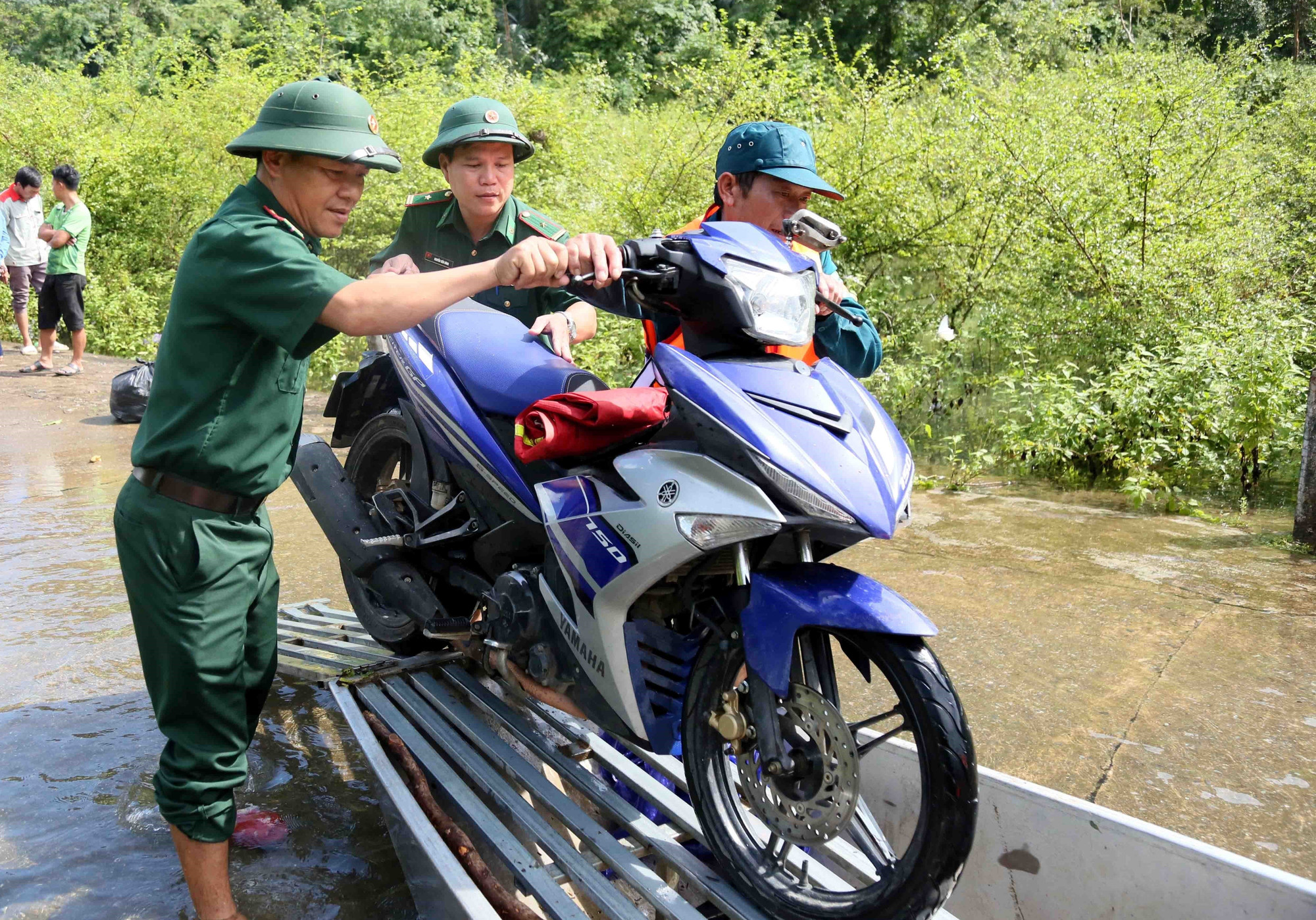 Cán bộ chiến sỹ Đồn Biên phòng Cà Xèng (Ban Chỉ huy Bộ đội Biên phòng Quảng Trị) hỗ trợ người dân đưa xe máy lên thuyền di chuyển qua đoạn ngập. Cán bộ chiến sỹ Đồn Biên phòng Cà Xèng (Ban Chỉ huy Bộ đội Biên phòng Quảng Trị) hỗ trợ người dân đưa xe máy lên thuyền di chuyển qua đoạn ngập.