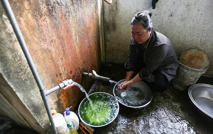 Bà Hoàng Thị Lý, khu tái định cư thôn Giếng Xạ, ngồi bên hai nguồn nước, một nguồn nước xanh ô nhiễm từ máy bơm của khu tái định cư và nguồn nước của người dân tự xin kéo về từ xã Tân Vinh kế bên. Ảnh: Trọng Đạt-TTXVN Người dân ngóng chờ nước tại khu tái định cư ở Hòa Bình ảnh 6