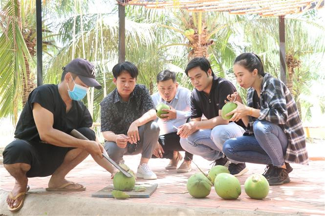 Du khách được nhân viên nông trại xanh Riverside Garden hướng dẫn cách bổ dừa. Ảnh: Chương Đài - TTXVN Đánh thức tiềm năng du lịch nơi 'Ba đảo dừa xanh' (Bài 1) ảnh 2