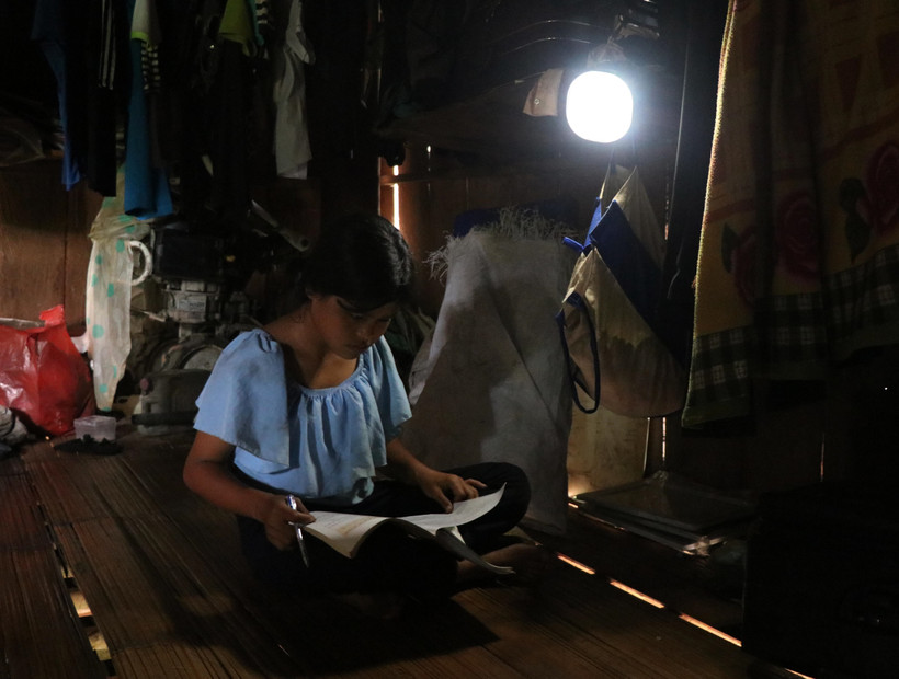 Em Đinh Thị Khơ, làng Mang Ve, học bài dưới ánh đèn năng lượng nguồn sáng yếu ớt. Ảnh: Phạm Cường-TTXVN T 