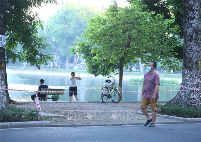 Nhiều người dân vẫn tập thể dục tại khu vực hồ Thiền Quang (Hà Nội) dù đã được lực lượng chức năng căng dây, cắm biển cấm . Ảnh: Hoàng Hiếu - TTXVN 