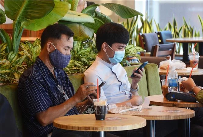 Khách hàng đeo khẩu trang khi uống cà phê tại quán. Ảnh: Văn Dũng - TTXVN