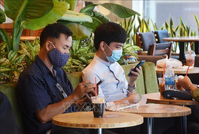 Khách hàng đeo khẩu trang khi uống cà phê tại quán. Ảnh: Văn Dũng - TTXVN