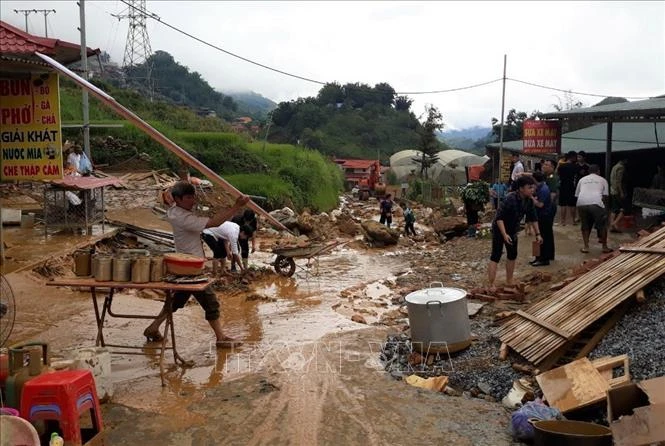 Lực lượng chức năng huy động trên 60 người cùng phương tiện, máy móc dọn mặt đường, tạm thời san lấp các điểm hư hỏng lớn để người dân đi lại. Ảnh: TTXVN/phát