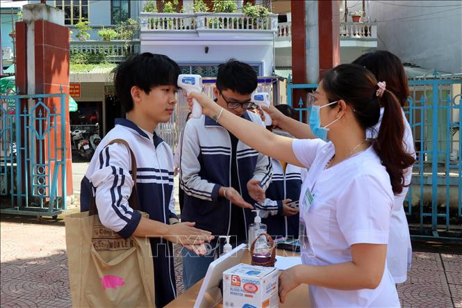 Các thí sinh được nhân viên y tế đo kiểm tra thân nhiệt và rửa tay sát khuẩn khi tới làm thủ tục tại điểm thi trường THPT Tô Hiệu, thành phố Sơn La . Ảnh: Hữu Quyết - TTXVN