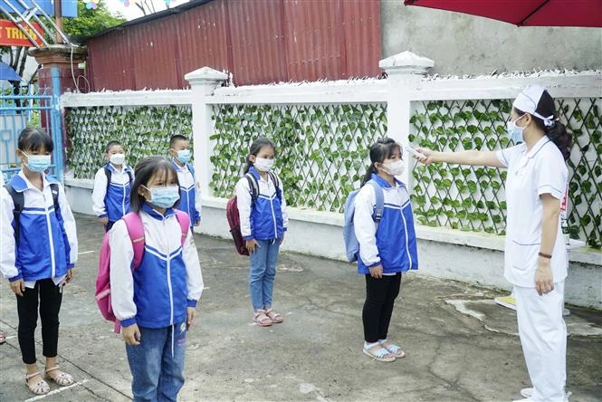 Cán bộ y tế đo thân nhiệt cho học sinh trường Tiểu học Thanh Xương, huyện Điện Biên trước khi vào lớp học. Ảnh: Xuân Tư – TTXVN 