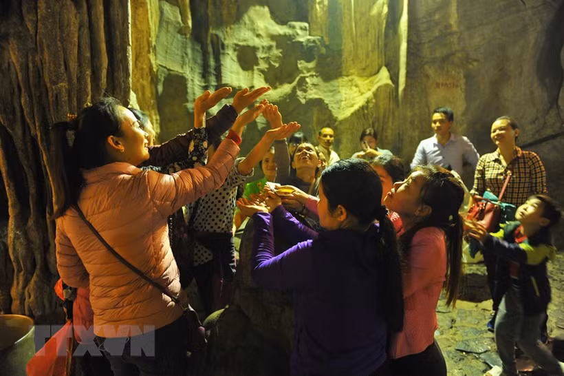 Các du khách đón những giọt nước từ nhũ đá trong động Hương Tích để cầu mong một năm mới nhiều sức khỏe, an lành và hạnh phúc. Ảnh: Minh Đức - TTXVN