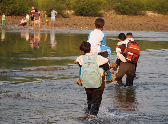 Người dân cõng con, cháu băng qua dòng nước chảy xiết để sang bờ đi học.