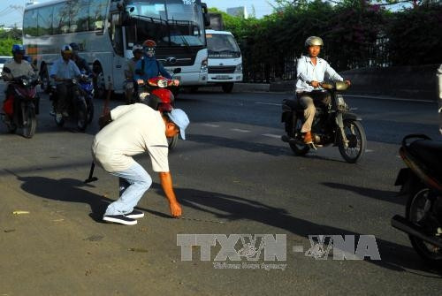 Anh Phong cần mẫn đi bộ trên quốc lộ hút từng chiếc đinh, mảnh thép để người đi đường không cán phải. Ảnh: Mạnh Linh - TTXVN