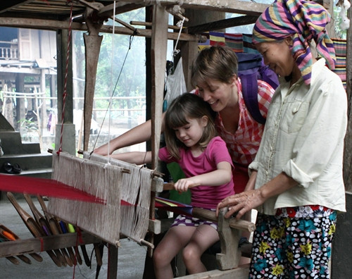 Du khách nước ngoài thích thú với việc được trải nghiệm nghề dệt thổ cẩm của dân tộc Thái. Ảnh: Nguyễn Thủy - TTXVN