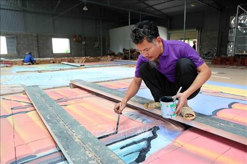 Nghệ nhân Lưu Xuân Khuyến đang hoàn thiện bức tranh gốm. Ảnh: Danh Lam - TTXVN