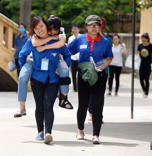 Sinh viên tình nguyện cõng thí sinh bị tai nạn gãy chân đến phòng thi taị điểm thi trường Cao đẳng Sư phạm Nghệ An. Ảnh: Thanh Tùng- TTXVN