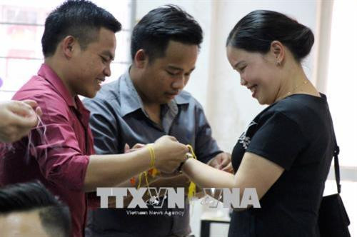 Lưu học sinh Lào buộc chỉ cổ tay cho khách đến tham dự Lễ chào mừng Tết cổ truyền Bunpimay. Ảnh: Diêp Anh - TTXVN Lưu học sinh Lào buộc chỉ cổ tay cho khách đến tham dự Lễ chào mừng Tết cổ truyền Bunpimay. Ảnh: Diêp Anh - TTXVN