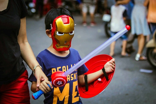Một em bé với bộ đồ chơi mặt nạ người sắt, gươm và chiếc khiên mang âm hưởng của bộ phim "Biệt đội siêu anh hùng"