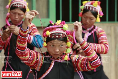 Chiếc vòng làm bằng nhựa màu nâu đỏ dùng để cố định những nếp tóc là lớp đầu tiên của khăn đội đầu người La Hủ. Lớp khăn thứ hai của chiếc khăn đội đầu của những người phụ nữ La Hủ. Nó được làm bằng vài nhiều màu và được gấp lại trước khi đội lên. Người phụ nữ La Hủ cố định lớp thứ 2 của chiếc khăn truyền thống. Sau khi đội lớp thứ 2, họ dùng dải dây thun vấn, che hết phần tóc còn lại. Lớp thứ 3 của chiếc khăn đội đầu có những sợi tua rua dài che phía sau đầu những người phụ nữ La Hủ. Thường từ lớp thứ 3 của chiếc khăn, họ cần một người khác giúp để hoàn thành chiếc khăn đội đầu sao cho đẹp nhất. Dải tua rua là lớp cuối cùng trên chiếc khăn đội đầu. Người con gái La Hủ luôn thường nuôi tóc dài để vấn tóc, đội chiếc khăn truyền thống rất cầu kỳ này. Chiếc khăn đội đầu của người phụ nữ La Hủ nhìn từ phía sau. Hai thế hệ phụ nữ người La Hủ ở Bum Tở. Vào ngày thường phụ nữ La Hủ mặc chiếc áo tà dài có màu đen truyền thống. Nhưng trong dịp lễ họ mặc thêm một chiếc áo khoác ngắn được đính trang trí khá cầu kỳ. Chiếc khăn đội đầu sặc sỡ là điểm nhấn làm nên sự khác biệt trong trang phục của người La Hủ. Những dải tua rua trên chiếc khăn đội đầu tạo nên nét rất sinh động trong trang phục của người phụ nữ La Hủ. Những cô gái La Hủ ở xã Bum Tở, huyện Mường Tè, tỉnh Lai Châu trong trang phục truyền thống đang tập múa, hát trong sân nhà văn hóa của bản.
