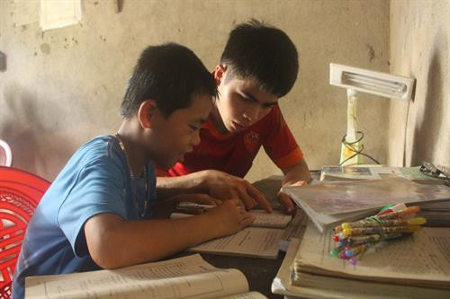 Lê Hữu Hiếu kèm em học bài. Ảnh: Khiếu Tư- TTXVN Lê Hữu Hiếu kèm em học bài. Ảnh: Khiếu Tư- TTXVN