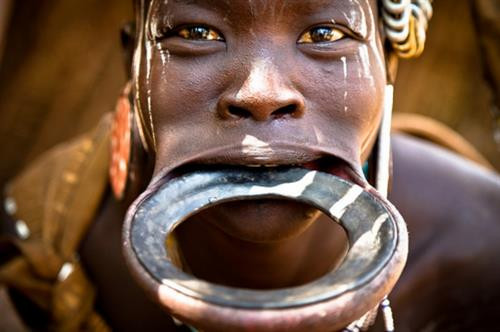 Bộ tộc Wodaabe: Bộ tộc này sống du canh du cư ở Niger, Nigeria, Cameroon, Chad... Cuối mỗi mùa mưa gần hồ Chad, người Wodaabe tổ chức Cure Salee - lễ hội của dân du mục. Hoạt động nổi bật nhất của lễ hội là cuộc thi sắc đẹp của các chàng trai. Họ mặc trang phục lộng lẫy nhất, trang điểm và đeo trang sức, đứng chờ các cô gái đánh giá. Răng và tròng mắt trắng được ca ngợi, do đó những người tham dự thường cố gắng cười hết cỡ. Ảnh: Daily Mail. Bộ tộc Mursi, Ethiopia: Môi dưới của phụ nữ trong bộ tộc được tạo lỗ từ khi còn nhỏ, sau đó lồng một chiếc đĩa gốm vào. Kích cỡ đĩa tăng dần theo thời gian và đĩa càng lớn càng được coi trọng. Ảnh: Sosyal Bilimler. Bộ tộc Himba, Namibia: Phụ nữ của tộc Himba nổi tiếng với tóc và làn da ánh đỏ. Họ bôi otjize - một hỗn hợp gồm bơ, mỡ và đất đỏ - lên tóc và da hàng ngày. Nhiều người cho rằng otjize giúp tránh nắng và chống côn trùng, nhưng tộc Himba cho biết họ dùng chúng chỉ hoàn toàn vì lý do thẩm mỹ. Ảnh: Frans Lanting. Bộ tộc Hamar, Ethiopia: Các chàng trai của tộc Hamar thực hiện nghi lễ nhảy bò để đánh dấu sự trưởng thành của mình. Mỗi người sẽ phải nhảy trên lưng những con bò bốn lượt để được công nhận quyền lấy vợ. Chỉ cần trượt chân là họ có thể bị thương. Ảnh: CNN. Bộ tộc Xhosa, Nam Phi: Khi đến tuổi trưởng thành, nam thanh niên tộc Xhosa sẽ phải trải qua một nghi lễ khắc nghiệt. Trước hết, họ sẽ được cắt bao quy đầu theo phương pháp truyền thống, sau đó phải rời khỏi làng với khuôn mặt bôi đất sét trắng, trùm chăn và đem theo ít đồ dùng thiết yếu. Họ phải sống trong khu dành riêng cho nghi lễ này và tự xoay xở trong hai tháng. Khi trở về, các chàng trai được công nhận là người trưởng thành và nhận một chiếc chăn mới. Ảnh: Voices of Africa. Bộ tộc Chewa: Sống rải rác ở Zambia, Zimbabwe, Malawi và Mozambique, bộ tộc này vẫn theo phương thức mẫu hệ từ xa xưa. Trong đó, tài sản và đất đai được truyền từ mẹ sang con gái. Tuy nhiên, đàn ông vẫn nắm quyền hành trong bộ tộc. Ảnh: CNN. Bộ tộc Maasai, Đông Phi: Nước bọt là một phần quan trọng trong đời sống của người Maasai ở Đông Phi. Loại dịch cơ thể này được coi là phước lành, tinh hoa của con người và việc nhổ nước bọt lên người khác là lời ban phước. Khi trẻ con ra đời, người trong bộ tộc sẽ nhổ nước bọt lên chúng để cầu mong chúng có cuộc sống may mắn. Khi có người đi xa, các bô lão sẽ nhổ lên đầu họ để chúc họ bình yên, an toàn. Ảnh: CNN. Bộ tộc Bodi, Ethiopia: Vào tháng sáu hoặc tháng bảy hàng năm ở thung lũng Oma, người Bodi lại tham dự cuộc thi có tên Ka’el. Trước đó nhiều tháng, nam giới tách ra sống riêng. Họ cố gắng uống thật nhiều sữa bò và huyết bò để tăng cân. Mỗi dòng họ sẽ cử một nam giới chưa vợ ra tranh danh hiệu người béo nhất. Người chiến thắng sẽ được vinh danh và có cơ hội lấy vợ dễ dàng hơn. Vài tuần sau cuộc thi, họ lại trở về với hình dáng cũ. Ảnh: Daily Mail. Bộ tộc Wodaabe: Bộ tộc này sống du canh du cư ở Niger, Nigeria, Cameroon, Chad... Cuối mỗi mùa mưa gần hồ Chad, người Wodaabe tổ chức Cure Salee - lễ hội của dân du mục. Hoạt động nổi bật nhất của lễ hội là cuộc thi sắc đẹp của các chàng trai. Họ mặc trang phục lộng lẫy nhất, trang điểm và đeo trang sức, đứng chờ các cô gái đánh giá. Răng và tròng mắt trắng được ca ngợi, do đó những người tham dự thường cố gắng cười hết cỡ. Ảnh: Daily Mail. Bộ tộc Mursi, Ethiopia: Môi dưới của phụ nữ trong bộ tộc được tạo lỗ từ khi còn nhỏ, sau đó lồng một chiếc đĩa gốm vào. Kích cỡ đĩa tăng dần theo thời gian và đĩa càng lớn càng được coi trọng. Ảnh: Sosyal Bilimler. Bộ tộc Himba, Namibia: Phụ nữ của tộc Himba nổi tiếng với tóc và làn da ánh đỏ. Họ bôi otjize - một hỗn hợp gồm bơ, mỡ và đất đỏ - lên tóc và da hàng ngày. Nhiều người cho rằng otjize giúp tránh nắng và chống côn trùng, nhưng tộc Himba cho biết họ dùng chúng chỉ hoàn toàn vì lý do thẩm mỹ. Ảnh: Frans Lanting. Bộ tộc Hamar, Ethiopia: Các chàng trai của tộc Hamar thực hiện nghi lễ nhảy bò để đánh dấu sự trưởng thành của mình. Mỗi người sẽ phải nhảy trên lưng những con bò bốn lượt để được công nhận quyền lấy vợ. Chỉ cần trượt chân là họ có thể bị thương. Ảnh: CNN. Bộ tộc Xhosa, Nam Phi: Khi đến tuổi trưởng thành, nam thanh niên tộc Xhosa sẽ phải trải qua một nghi lễ khắc nghiệt. Trước hết, họ sẽ được cắt bao quy đầu theo phương pháp truyền thống, sau đó phải rời khỏi làng với khuôn mặt bôi đất sét trắng, trùm chăn và đem theo ít đồ dùng thiết yếu. Họ phải sống trong khu dành riêng cho nghi lễ này và tự xoay xở trong hai tháng. Khi trở về, các chàng trai được công nhận là người trưởng thành và nhận một chiếc chăn mới. Ảnh: Voices of Africa. Bộ tộc Chewa: Sống rải rác ở Zambia, Zimbabwe, Malawi và Mozambique, bộ tộc này vẫn theo phương thức mẫu hệ từ xa xưa. Trong đó, tài sản và đất đai được truyền từ mẹ sang con gái. Tuy nhiên, đàn ông vẫn nắm quyền hành trong bộ tộc. Ảnh: CNN. Bộ tộc Maasai, Đông Phi: Nước bọt là một phần quan trọng trong đời sống của người Maasai ở Đông Phi. Loại dịch cơ thể này được coi là phước lành, tinh hoa của con người và việc nhổ nước bọt lên người khác là lời ban phước. Khi trẻ con ra đời, người trong bộ tộc sẽ nhổ nước bọt lên chúng để cầu mong chúng có cuộc sống may mắn. Khi có người đi xa, các bô lão sẽ nhổ lên đầu họ để chúc họ bình yên, an toàn. Ảnh: CNN. Bộ tộc Bodi, Ethiopia: Vào tháng sáu hoặc tháng bảy hàng năm ở thung lũng Oma, người Bodi lại tham dự cuộc thi có tên Ka’el. Trước đó nhiều tháng, nam giới tách ra sống riêng. Họ cố gắng uống thật nhiều sữa bò và huyết bò để tăng cân. Mỗi dòng họ sẽ cử một nam giới chưa vợ ra tranh danh hiệu người béo nhất. Người chiến thắng sẽ được vinh danh và có cơ hội lấy vợ dễ dàng hơn. Vài tuần sau cuộc thi, họ lại trở về với hình dáng cũ. Ảnh: Daily Mail.