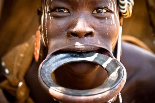 Bộ tộc Wodaabe: Bộ tộc này sống du canh du cư ở Niger, Nigeria, Cameroon, Chad... Cuối mỗi mùa mưa gần hồ Chad, người Wodaabe tổ chức Cure Salee - lễ hội của dân du mục. Hoạt động nổi bật nhất của lễ hội là cuộc thi sắc đẹp của các chàng trai. Họ mặc trang phục lộng lẫy nhất, trang điểm và đeo trang sức, đứng chờ các cô gái đánh giá. Răng và tròng mắt trắng được ca ngợi, do đó những người tham dự thường cố gắng cười hết cỡ. Ảnh: Daily Mail. Bộ tộc Mursi, Ethiopia: Môi dưới của phụ nữ trong bộ tộc được tạo lỗ từ khi còn nhỏ, sau đó lồng một chiếc đĩa gốm vào. Kích cỡ đĩa tăng dần theo thời gian và đĩa càng lớn càng được coi trọng. Ảnh: Sosyal Bilimler. Bộ tộc Himba, Namibia: Phụ nữ của tộc Himba nổi tiếng với tóc và làn da ánh đỏ. Họ bôi otjize - một hỗn hợp gồm bơ, mỡ và đất đỏ - lên tóc và da hàng ngày. Nhiều người cho rằng otjize giúp tránh nắng và chống côn trùng, nhưng tộc Himba cho biết họ dùng chúng chỉ hoàn toàn vì lý do thẩm mỹ. Ảnh: Frans Lanting. Bộ tộc Hamar, Ethiopia: Các chàng trai của tộc Hamar thực hiện nghi lễ nhảy bò để đánh dấu sự trưởng thành của mình. Mỗi người sẽ phải nhảy trên lưng những con bò bốn lượt để được công nhận quyền lấy vợ. Chỉ cần trượt chân là họ có thể bị thương. Ảnh: CNN. Bộ tộc Xhosa, Nam Phi: Khi đến tuổi trưởng thành, nam thanh niên tộc Xhosa sẽ phải trải qua một nghi lễ khắc nghiệt. Trước hết, họ sẽ được cắt bao quy đầu theo phương pháp truyền thống, sau đó phải rời khỏi làng với khuôn mặt bôi đất sét trắng, trùm chăn và đem theo ít đồ dùng thiết yếu. Họ phải sống trong khu dành riêng cho nghi lễ này và tự xoay xở trong hai tháng. Khi trở về, các chàng trai được công nhận là người trưởng thành và nhận một chiếc chăn mới. Ảnh: Voices of Africa. Bộ tộc Chewa: Sống rải rác ở Zambia, Zimbabwe, Malawi và Mozambique, bộ tộc này vẫn theo phương thức mẫu hệ từ xa xưa. Trong đó, tài sản và đất đai được truyền từ mẹ sang con gái. Tuy nhiên, đàn ông vẫn nắm quyền hành trong bộ tộc. Ảnh: CNN. Bộ tộc Maasai, Đông Phi: Nước bọt là một phần quan trọng trong đời sống của người Maasai ở Đông Phi. Loại dịch cơ thể này được coi là phước lành, tinh hoa của con người và việc nhổ nước bọt lên người khác là lời ban phước. Khi trẻ con ra đời, người trong bộ tộc sẽ nhổ nước bọt lên chúng để cầu mong chúng có cuộc sống may mắn. Khi có người đi xa, các bô lão sẽ nhổ lên đầu họ để chúc họ bình yên, an toàn. Ảnh: CNN. Bộ tộc Bodi, Ethiopia: Vào tháng sáu hoặc tháng bảy hàng năm ở thung lũng Oma, người Bodi lại tham dự cuộc thi có tên Ka’el. Trước đó nhiều tháng, nam giới tách ra sống riêng. Họ cố gắng uống thật nhiều sữa bò và huyết bò để tăng cân. Mỗi dòng họ sẽ cử một nam giới chưa vợ ra tranh danh hiệu người béo nhất. Người chiến thắng sẽ được vinh danh và có cơ hội lấy vợ dễ dàng hơn. Vài tuần sau cuộc thi, họ lại trở về với hình dáng cũ. Ảnh: Daily Mail.