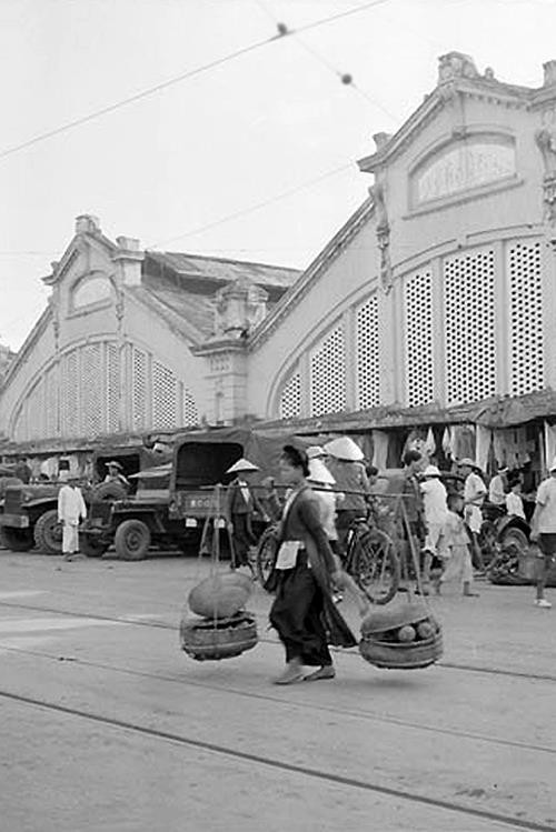 Một phụ nữ gánh hàng trước chợ đầu thập niên 1950. Ảnh: Flickr.