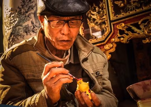 Nghệ nhân Phùng Đình Giáp đang tô những đường nét cuối cùng cho phỗng lợn đất. Ảnh: vietnammoi.vn
