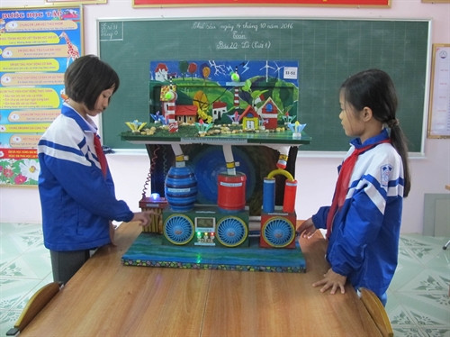 Em Đinh Quỳnh Ngân và Đinh Thị Nguyệt Minh bên mô hình máy thu và xử lý bão trong lòng đất. Ảnh: Thùy Dung - TTXVN