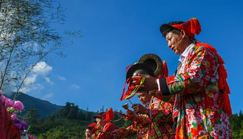 Bàn thờ treo bộ tranh thờ “Tam thanh” - 3 vị thần trong tín ngưỡng người Dao cai quản 3 nơi là Ngọc thanh (thần cai quản trên trời), Thượng thanh (thần cai quản trần gian) và Thái thanh (thần cai quản âm phủ). Theo truyền thuyết, tuy là vua nhưng Bàn Vương vẫn giữ thói quen sống giản dị, gần gũi với thiên nhiên. Ngài luôn căn dặn các con phải chăm chỉ lao động sản xuất. Có một lần, Bàn Vương cùng tùy tùng lên núi săn bắn, đuổi theo một con sơn dương bị thương, chẳng may bị sơn dương húc, ngài ngã vào cây gù hương và mất tại đó. Thi thể Bàn Vương bị vướng trên nhành cây, các con bèn chặt cây làm thân trống, đuổi bắt con sơn dương để lấy da làm trống tế lễ Bàn Vương. Từ đó. cứ đến khoảng tháng 2 Âm lịch hàng năm, con cháu người Dao từ đời này sang đời khác phải nhớ ngày cúng giỗ Bàn Vương, thể hiện sự biết ơn với tổ tiên đã sinh ra họ. Người dân các thôn chuẩn bị lễ vật, chờ đến giờ tốt để dâng lên Bàn Vương. Các thầy cúng bắt đầu thay lễ phục, giúp nhau sửa soạn mũ áo. Chân dung một trong số sáu thầy cúng của buổi lễ. Ông Triệu Chòi Quyên, thầy cúng trong xã, cho biết: "Các thầy cúng sẽ hát những bài ca cúng để nhờ thần linh, thổ địa nghênh đón Bàn Vương xuống đàn, nhận lễ vật của con cháu dâng lên". Sau mỗi lời khấn bằng tiếng Dao, thầy cúng và người dân các thôn cùng quỳ lạy Bàn Vương. Các điệu múa chuông, múa bắt rùa... lần lượt được các thầy cúng thực hiện sau khi mời để tái hiện lại tiểu sử của Bàn Vương năm xưa như vóc dáng, cách hái lượm săn bắn. Việc này theo các thầy cúng vừa để thể hiện ý chí, sức mạnh sinh tồn của người xưa, vừa để nhắc nhở con cháu ngày nay cần cù, chịu khó làm ăn như cha ông trước đây. Theo ông Quyên, vật chày là một trò chơi dân gian thể hiện sức mạnh, sự kết hợp khéo léo, sự bí ẩn của cả người gánh và người vật. Sau khi thầy cúng làm phép nhờ thần linh giúp đỡ, dù rất đông người cùng tham gia nhưng không thể ấn nổi đầu chày chạm đất. Điều này thể hiện việc bản làng năm đó được các vị thần phù hộ, nâng đỡ. Người dân tới dâng lễ và tham gia lễ hội Bàn Vương. Bàn thờ treo bộ tranh thờ “Tam thanh” - 3 vị thần trong tín ngưỡng người Dao cai quản 3 nơi là Ngọc thanh (thần cai quản trên trời), Thượng thanh (thần cai quản trần gian) và Thái thanh (thần cai quản âm phủ). Theo truyền thuyết, tuy là vua nhưng Bàn Vương vẫn giữ thói quen sống giản dị, gần gũi với thiên nhiên. Ngài luôn căn dặn các con phải chăm chỉ lao động sản xuất. Có một lần, Bàn Vương cùng tùy tùng lên núi săn bắn, đuổi theo một con sơn dương bị thương, chẳng may bị sơn dương húc, ngài ngã vào cây gù hương và mất tại đó. Thi thể Bàn Vương bị vướng trên nhành cây, các con bèn chặt cây làm thân trống, đuổi bắt con sơn dương để lấy da làm trống tế lễ Bàn Vương. Từ đó. cứ đến khoảng tháng 2 Âm lịch hàng năm, con cháu người Dao từ đời này sang đời khác phải nhớ ngày cúng giỗ Bàn Vương, thể hiện sự biết ơn với tổ tiên đã sinh ra họ. Người dân các thôn chuẩn bị lễ vật, chờ đến giờ tốt để dâng lên Bàn Vương. Các thầy cúng bắt đầu thay lễ phục, giúp nhau sửa soạn mũ áo. Chân dung một trong số sáu thầy cúng của buổi lễ. Ông Triệu Chòi Quyên, thầy cúng trong xã, cho biết: "Các thầy cúng sẽ hát những bài ca cúng để nhờ thần linh, thổ địa nghênh đón Bàn Vương xuống đàn, nhận lễ vật của con cháu dâng lên". Sau mỗi lời khấn bằng tiếng Dao, thầy cúng và người dân các thôn cùng quỳ lạy Bàn Vương. Các điệu múa chuông, múa bắt rùa... lần lượt được các thầy cúng thực hiện sau khi mời để tái hiện lại tiểu sử của Bàn Vương năm xưa như vóc dáng, cách hái lượm săn bắn. Việc này theo các thầy cúng vừa để thể hiện ý chí, sức mạnh sinh tồn của người xưa, vừa để nhắc nhở con cháu ngày nay cần cù, chịu khó làm ăn như cha ông trước đây. Theo ông Quyên, vật chày là một trò chơi dân gian thể hiện sức mạnh, sự kết hợp khéo léo, sự bí ẩn của cả người gánh và người vật. Sau khi thầy cúng làm phép nhờ thần linh giúp đỡ, dù rất đông người cùng tham gia nhưng không thể ấn nổi đầu chày chạm đất. Điều này thể hiện việc bản làng năm đó được các vị thần phù hộ, nâng đỡ. Người dân tới dâng lễ và tham gia lễ hội Bàn Vương.