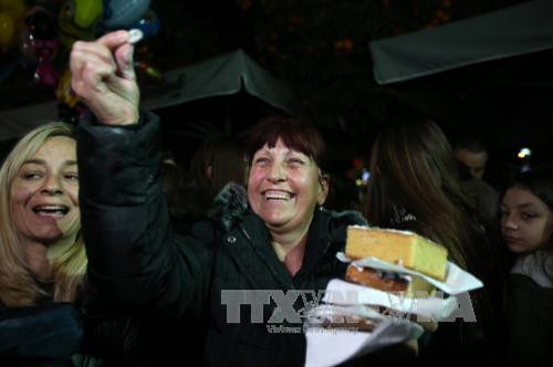 Người phụ nữ vui sướng khoe "đồng xu may mắn" trong phần bánh mình được chia. Ảnh THX/TTXVN Người phụ nữ vui sướng khoe "đồng xu may mắn" trong phần bánh mình được chia. Ảnh THX/TTXVN