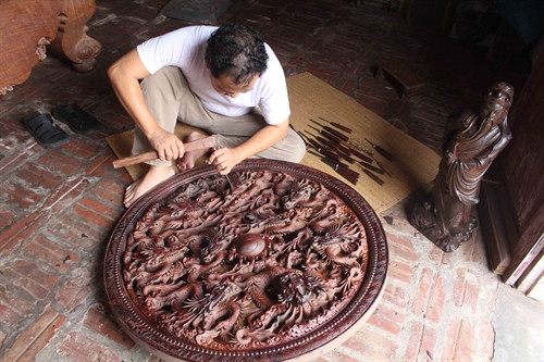 Nghệ nhân Nguyễn Ngọc Kha chạm bức tranh Cửu long chầu nguyệt. Ảnh: Thanh Thương - TTXVN