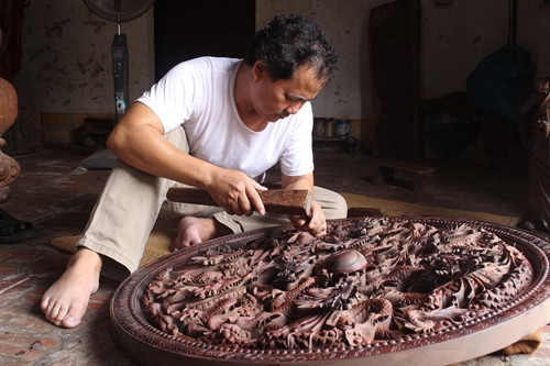 Nghệ nhân Nguyễn Ngọc Kha chạm bức tranh Cửu long chầu nguyệt. Ảnh: Thanh Thương - TTXVN