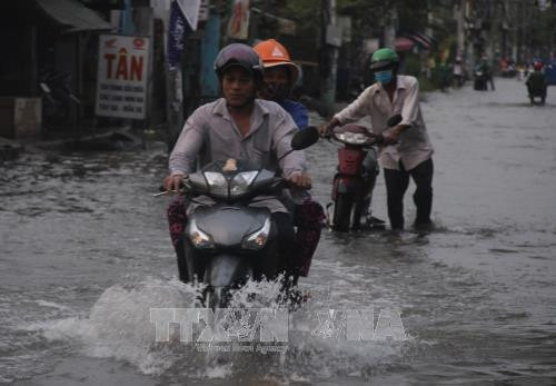 Người dân cố gắng điều khiển xe máy chạy qua đoạn ngập nước trên đường Lê Văn Lương, huyện Nhà Bè. Ảnh: Xuân Dự - TTXVN