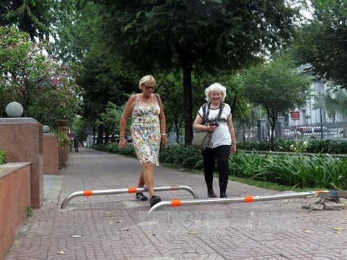 Du khách đi bộ trên vỉa hè vừa lắp các thanh barie tuyến đường Lý Tự Trọng. Ảnh: Hoàng Hải - TTXVN