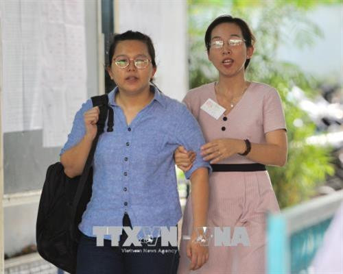 Thí sinh Nguyễn Thị Minh Thư (trái) bị khuyết tật mắt được giám thị hỗ trợ tại một điểm thi Thành phố Hồ Chí Minh. Ảnh: Quang Nhựt - TTXVN