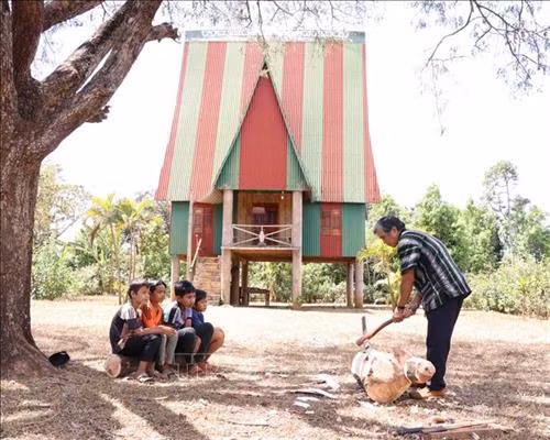 Nghệ nhân ưu tú Ksor Krôh hướng dẫn các em nhỏ tạc tượng gỗ. Ảnh: Hồng Điệp - TTXVN