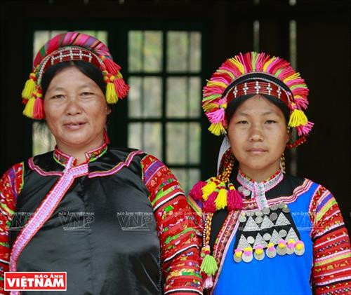 Chiếc vòng làm bằng nhựa màu nâu đỏ dùng để cố định những nếp tóc là lớp đầu tiên của khăn đội đầu người La Hủ. Lớp khăn thứ hai của chiếc khăn đội đầu của những người phụ nữ La Hủ. Nó được làm bằng vài nhiều màu và được gấp lại trước khi đội lên. Người phụ nữ La Hủ cố định lớp thứ 2 của chiếc khăn truyền thống. Sau khi đội lớp thứ 2, họ dùng dải dây thun vấn, che hết phần tóc còn lại. Lớp thứ 3 của chiếc khăn đội đầu có những sợi tua rua dài che phía sau đầu những người phụ nữ La Hủ. Thường từ lớp thứ 3 của chiếc khăn, họ cần một người khác giúp để hoàn thành chiếc khăn đội đầu sao cho đẹp nhất. Dải tua rua là lớp cuối cùng trên chiếc khăn đội đầu. Người con gái La Hủ luôn thường nuôi tóc dài để vấn tóc, đội chiếc khăn truyền thống rất cầu kỳ này. Chiếc khăn đội đầu của người phụ nữ La Hủ nhìn từ phía sau. Hai thế hệ phụ nữ người La Hủ ở Bum Tở. Vào ngày thường phụ nữ La Hủ mặc chiếc áo tà dài có màu đen truyền thống. Nhưng trong dịp lễ họ mặc thêm một chiếc áo khoác ngắn được đính trang trí khá cầu kỳ. Chiếc khăn đội đầu sặc sỡ là điểm nhấn làm nên sự khác biệt trong trang phục của người La Hủ. Những dải tua rua trên chiếc khăn đội đầu tạo nên nét rất sinh động trong trang phục của người phụ nữ La Hủ. Những cô gái La Hủ ở xã Bum Tở, huyện Mường Tè, tỉnh Lai Châu trong trang phục truyền thống đang tập múa, hát trong sân nhà văn hóa của bản.