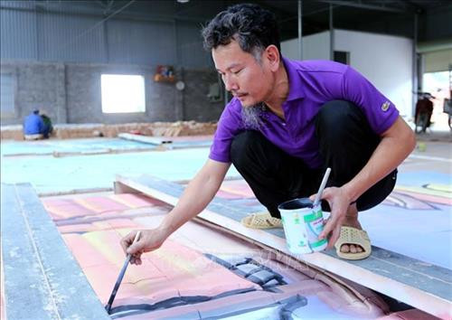 Nghệ nhân Lưu Xuân Khuyến đang hoàn thiện bức tranh gốm. Ảnh: Danh Lam - TTXVN