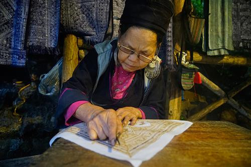 Việc đầu tiên phụ nữ Mông làm là thu hoạch cây lanh và được phơi thành những đụm to ở bất cứ khoảng đất rộng nào. Khi lanh đã đủ khô được mang về nhà, tước vỏ... …tiếp đó là giã lanh và nối sợi. Đây là công đoạn vất vả và tốn nhiều công sức nhất, sau khi giã cho mềm là tỉ mẩn nối những sợi lanh sao cho đều và đẹp. Phụ nữ Mông luôn tranh thủ trên đường lên nương, xuống chợ hay bất cứ khi nào, miễn đôi tay được "rảnh" là lại thoăn thoắt nối sợi, cuộn thành những búi nhỏ ở tay. Sau khi se và nối sợi bằng tay, sợi được đưa lên guồng se tiếp một lần nữa rồi cho vào guồng thu sợi. Qua các công đoạn sơ chế, sợi có màu trắng, mịn, dai và tiếp tục lăn mỏng, phẳng hơn, sau đó được xếp thành con chỉ dệt và dệt thành vải. Để tạo hoa văn, họa tiết, người Mông thường dùng kỹ thuật vẽ sáp ong do những người lớn tuổi có kinh nghiệm lâu năm thực hiện. Nhuộm chàm là công đoạn không thể thiếu. Sau khi nhuộm chàm, những tấm vải được phơi khô và giặt tẩy sáp... ... tiếp tục giặt nhiều lần rồi lăn để tạo độ phẳng và mịn. Những tấm vải thổ cẩm hoàn thành chứa đựng trong đó bao mồ hôi, công sức của phụ nữ Mông. Việc đầu tiên phụ nữ Mông làm là thu hoạch cây lanh và được phơi thành những đụm to ở bất cứ khoảng đất rộng nào. Khi lanh đã đủ khô được mang về nhà, tước vỏ... …tiếp đó là giã lanh và nối sợi. Đây là công đoạn vất vả và tốn nhiều công sức nhất, sau khi giã cho mềm là tỉ mẩn nối những sợi lanh sao cho đều và đẹp. Phụ nữ Mông luôn tranh thủ trên đường lên nương, xuống chợ hay bất cứ khi nào, miễn đôi tay được "rảnh" là lại thoăn thoắt nối sợi, cuộn thành những búi nhỏ ở tay. Sau khi se và nối sợi bằng tay, sợi được đưa lên guồng se tiếp một lần nữa rồi cho vào guồng thu sợi. Qua các công đoạn sơ chế, sợi có màu trắng, mịn, dai và tiếp tục lăn mỏng, phẳng hơn, sau đó được xếp thành con chỉ dệt và dệt thành vải. Để tạo hoa văn, họa tiết, người Mông thường dùng kỹ thuật vẽ sáp ong do những người lớn tuổi có kinh nghiệm lâu năm thực hiện. Nhuộm chàm là công đoạn không thể thiếu. Sau khi nhuộm chàm, những tấm vải được phơi khô và giặt tẩy sáp... ... tiếp tục giặt nhiều lần rồi lăn để tạo độ phẳng và mịn. Những tấm vải thổ cẩm hoàn thành chứa đựng trong đó bao mồ hôi, công sức của phụ nữ Mông.