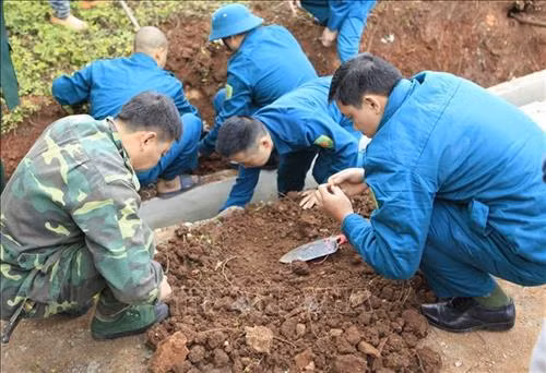 Lực lượng Dân quân tiến hành khai quật hài cốt. Ảnh: Xuân Tư - TTXVN