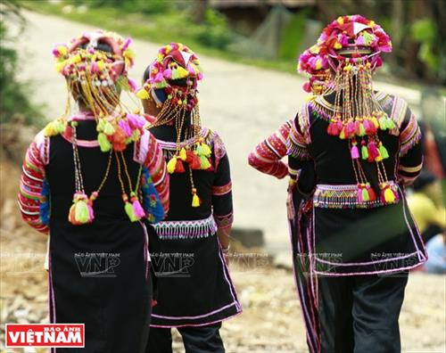 Chiếc vòng làm bằng nhựa màu nâu đỏ dùng để cố định những nếp tóc là lớp đầu tiên của khăn đội đầu người La Hủ. Lớp khăn thứ hai của chiếc khăn đội đầu của những người phụ nữ La Hủ. Nó được làm bằng vài nhiều màu và được gấp lại trước khi đội lên. Người phụ nữ La Hủ cố định lớp thứ 2 của chiếc khăn truyền thống. Sau khi đội lớp thứ 2, họ dùng dải dây thun vấn, che hết phần tóc còn lại. Lớp thứ 3 của chiếc khăn đội đầu có những sợi tua rua dài che phía sau đầu những người phụ nữ La Hủ. Thường từ lớp thứ 3 của chiếc khăn, họ cần một người khác giúp để hoàn thành chiếc khăn đội đầu sao cho đẹp nhất. Dải tua rua là lớp cuối cùng trên chiếc khăn đội đầu. Người con gái La Hủ luôn thường nuôi tóc dài để vấn tóc, đội chiếc khăn truyền thống rất cầu kỳ này. Chiếc khăn đội đầu của người phụ nữ La Hủ nhìn từ phía sau. Hai thế hệ phụ nữ người La Hủ ở Bum Tở. Vào ngày thường phụ nữ La Hủ mặc chiếc áo tà dài có màu đen truyền thống. Nhưng trong dịp lễ họ mặc thêm một chiếc áo khoác ngắn được đính trang trí khá cầu kỳ. Chiếc khăn đội đầu sặc sỡ là điểm nhấn làm nên sự khác biệt trong trang phục của người La Hủ. Những dải tua rua trên chiếc khăn đội đầu tạo nên nét rất sinh động trong trang phục của người phụ nữ La Hủ. Những cô gái La Hủ ở xã Bum Tở, huyện Mường Tè, tỉnh Lai Châu trong trang phục truyền thống đang tập múa, hát trong sân nhà văn hóa của bản.