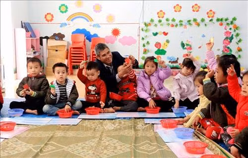 Ông Ma Kim Hải cùng với các cháu học sinh tại điểm trường mầm non thôn Cả. Ảnh: TTXVN