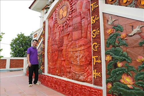 Nghệ nhân Lưu Xuân Khuyến bên sản phẩm tranh gốm tường khổ lớn của mình. Ảnh: Thành Đạt – TTXVN