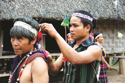 Người đàn ông Cơ-tu đang nhờ con trai làm đẹp cho mình để chuẩn bị vào hội và vật không thể thiếu là những chuỗi vòng đeo cổ