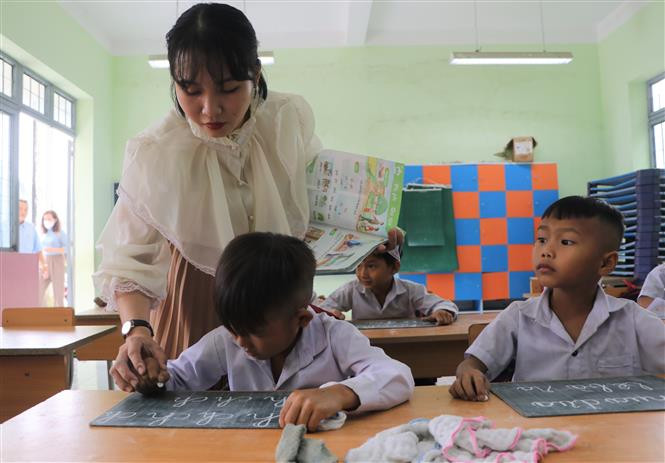 Cô giáo Nguyễn Thị Ý Mỹ cầm tay nắn từng nét chữ cho học sinh. Ảnh: Đinh Hương - TTXVN Ngày Nhà giáo Việt Nam 20/11: Cha và con thầy giáo cùng hành trình "gieo chữ" nơi vùng cao Trà Bồng ảnh 4
