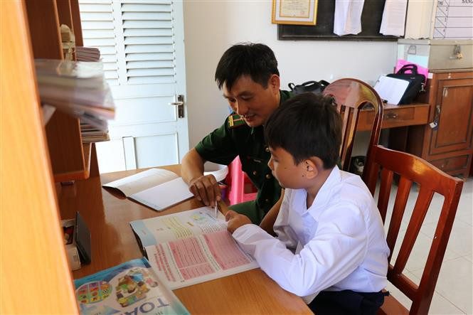 Thiếu tá chuyên nghiệp Trần Văn Ánh (Đồn Biên phòng Phú Tân, Bộ đội Biên phòng Tiền Giang) hướng dẫn em Võ Vũ Trường Giang học bài. Em Giang được Đồn Biên phòng Phú Tân nhận nuôi đến hết lớp 9 và hỗ trợ học hết lớp 12 theo chương trình “Nâng bước em tới trường” bằng nguồn kinh phí do cán bộ, chiến sĩ đơn vị tự nguyện đóng góp hỗ trợ. Ảnh: Hữu Chí – TTXVN “Gần dân, sát dân” (Bài 1) ảnh 6