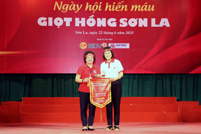 Phó Giám đốc Trung tâm Máu quốc gia (Viện Huyết học - Truyền máu Trung ương) Võ Thị Diễm Hà (bên phải) trao cờ lưu niệm và biểu trưng đơn vị tổ chức Chương trình Hành trình đỏ cho Chủ tịch Hội Chữ thập đỏ tỉnh Sơn La Cầm Thị Chuyên. potal-ngay-hoi-hien-mau-giot-hong-son-la-nam-2025-8106653.jpg